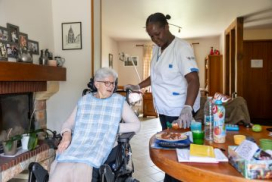 photo montrant une personne âgée et son aide à domicile lors de la préparation d'un repas, dans un salle à manger, près d'une cheminée
