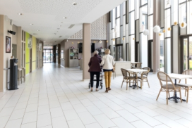 photo montrant l'accueil d'un ehpad avec des tables, des chaises et des personnes qui marchent de dos