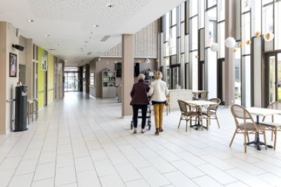 photo montrant l'accueil d'un ehpad avec des tables, des chaises et des personnes qui marchent